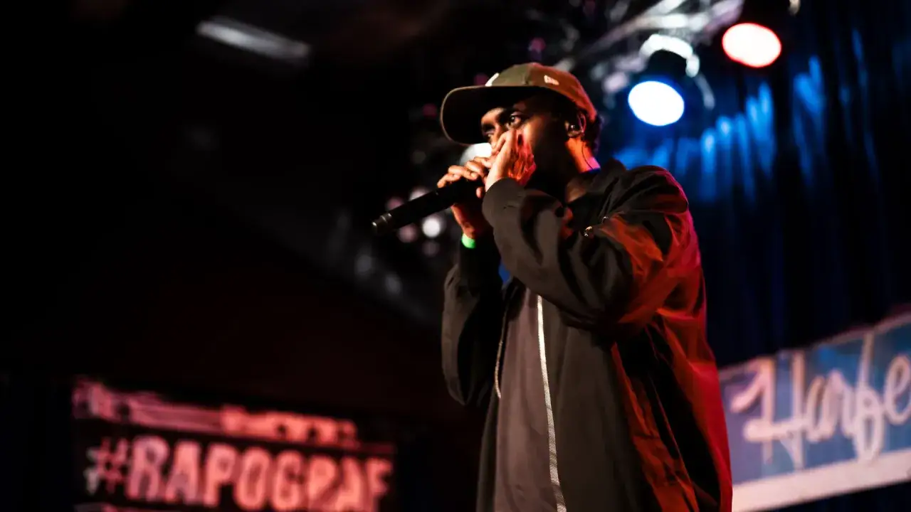 Ein Hip-Hop-Künstler mit Mikrofon auf der Bühne, beleuchtet von Bühnenlichtern.