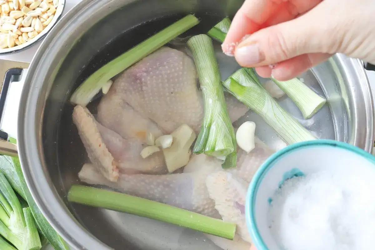 Se a&ntilde;ade sal a un pollo entero en una olla con cebolleta, apio y ajo, preparando un delicioso caldo de gallina.