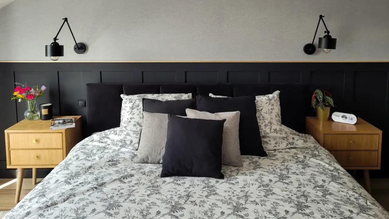 Elegancka sypialnia z czarną boazerią angielską, łóżkiem z wieloma poduszkami i kwiecistą pościelą.