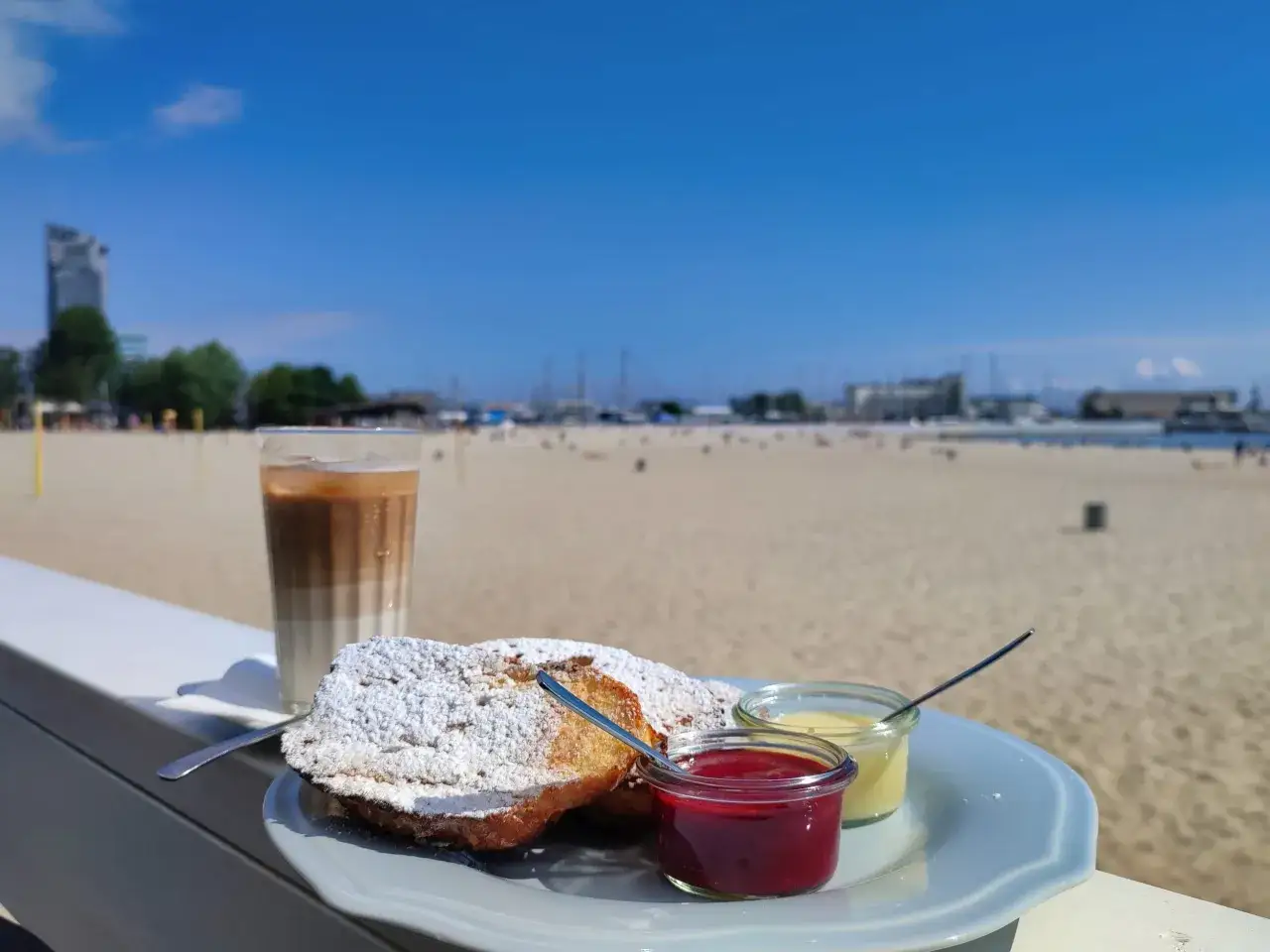 Słodkie śniadanie w Gdyni: francuskie tosty z dżemem i kremem, kawa mrożona na tle plaży i morza.
