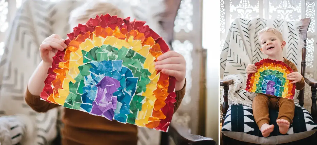 Kleiner Junge h&auml;lt stolz sein selbstgebasteltes Regenbogen-Kunstwerk. Die bunten Papierfetzen leuchten in Rot, Orange, Gelb, Gr&uuml;n, Blau und Violett.