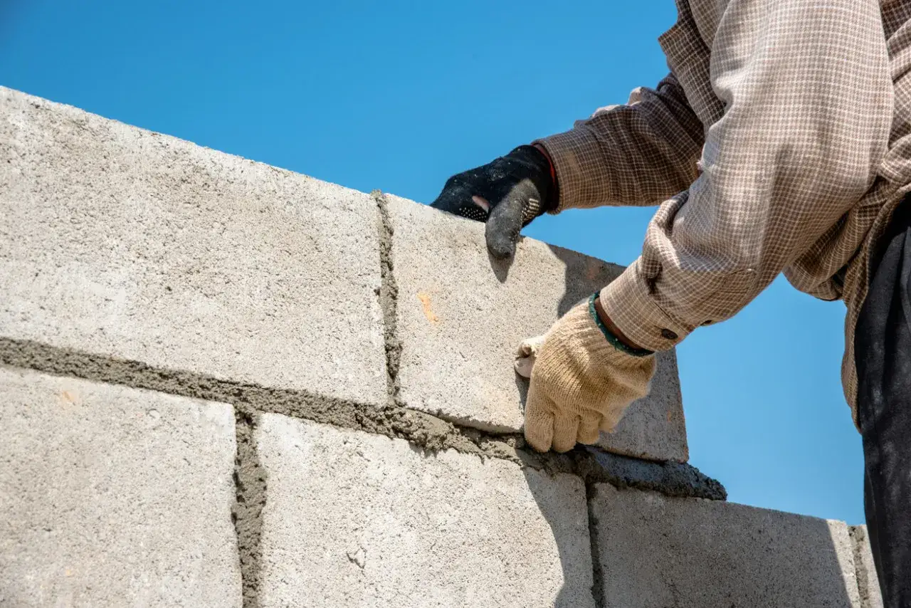 Un maçon pose une brique sur un mur en parpaings. La question est : peut-on fixer quelque chose sur un mur mitoyen ?