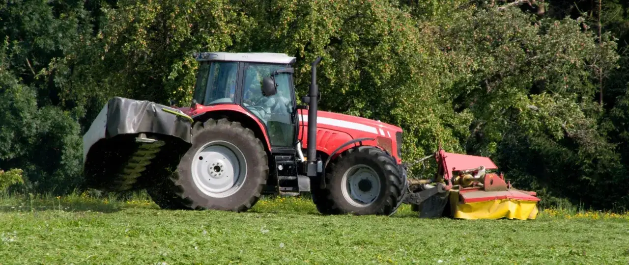 Czerwony traktor z kosiarką pracuje na łące, symbolizując rozwój małych gospodarstw 2025.
