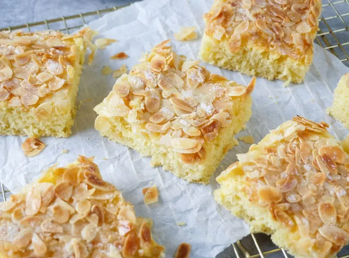 Saftiger Buttermilch Kuchen mit knusprigen Mandelblättchen und Zucker bestreut, auf Backpapier und einem Gitterrost angerichtet.