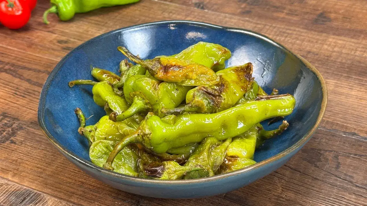 Friggitelli in padella, verdi e leggermente abbrustoliti, serviti in una ciotola blu su un tavolo di legno.