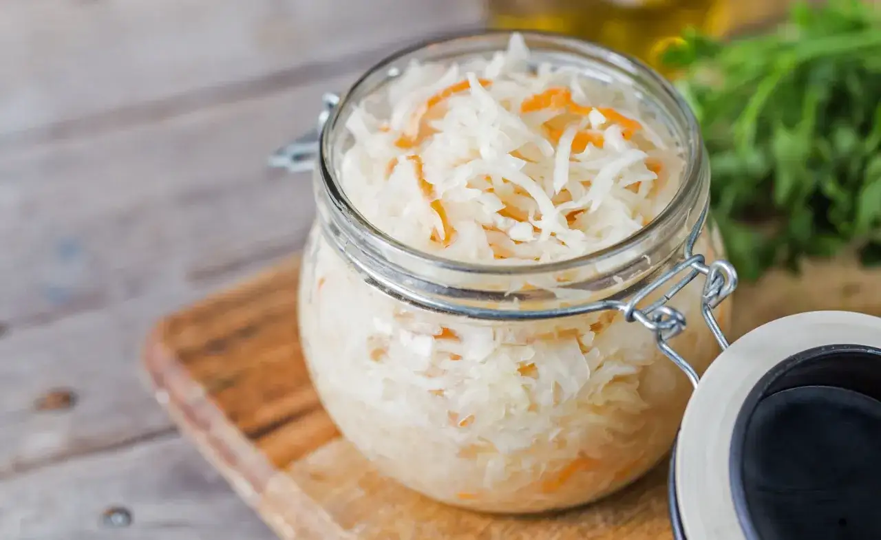 Ein Glas voller Sauerkrautsaft, basisch und gesund. Frisches Kraut mit Karottenstreifen, bereit zur Fermentation.