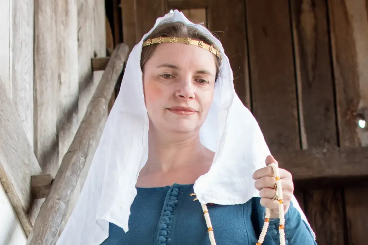 Frau mit mittelalterlichem Make-up, goldenem Stirnband und wei&szlig;em Schleier, h&auml;lt eine Perlenkette.