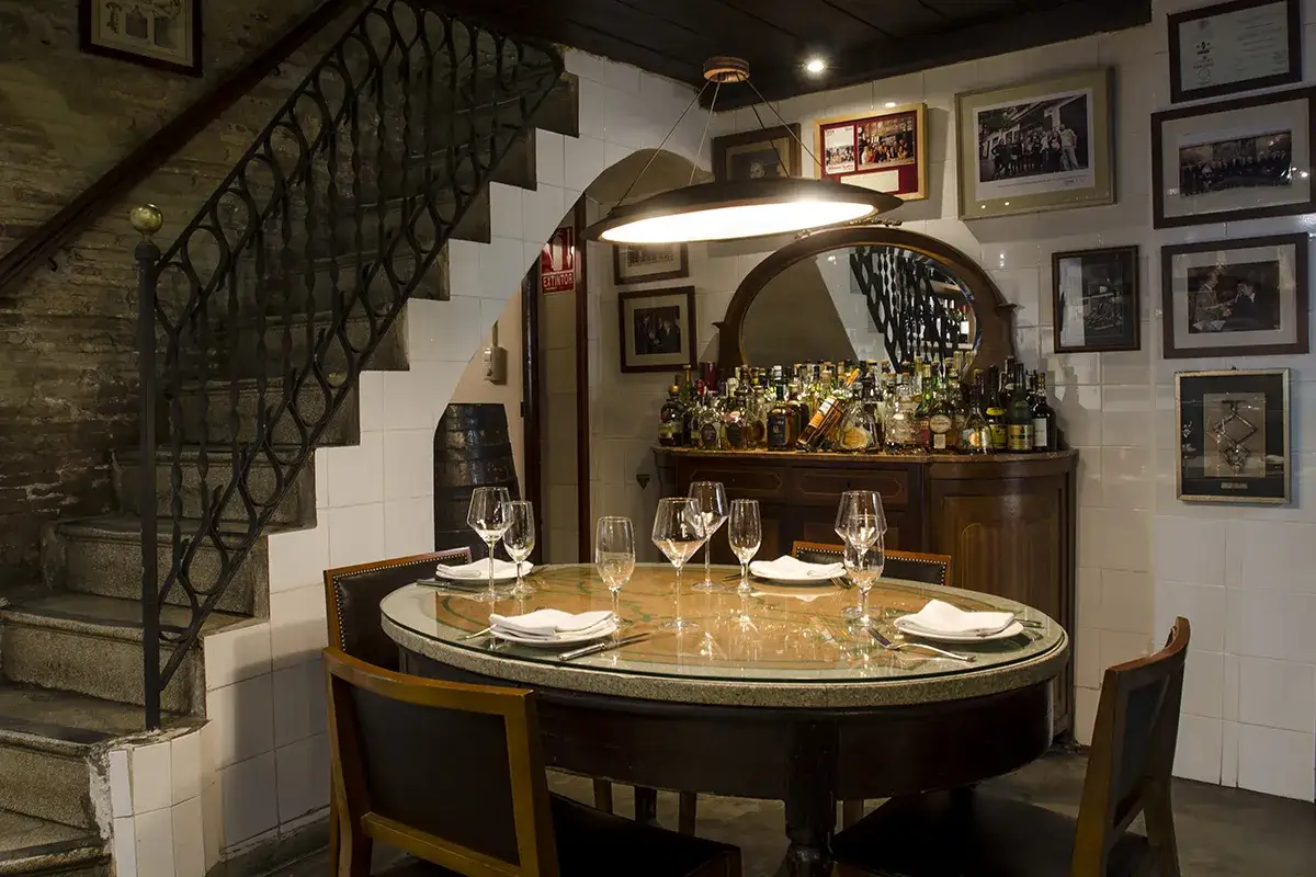 Elegante mesa puesta en un rincón acogedor de una casa montaña en Valencia, con una escalera de piedra y bar a la vista.
