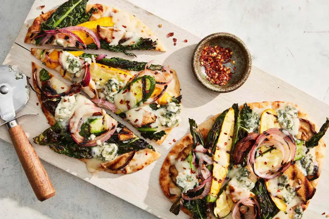 Pyszna pizza wegetariańska z grillowanymi warzywami, cebulą i serem pleśniowym, posypana płatkami chili.