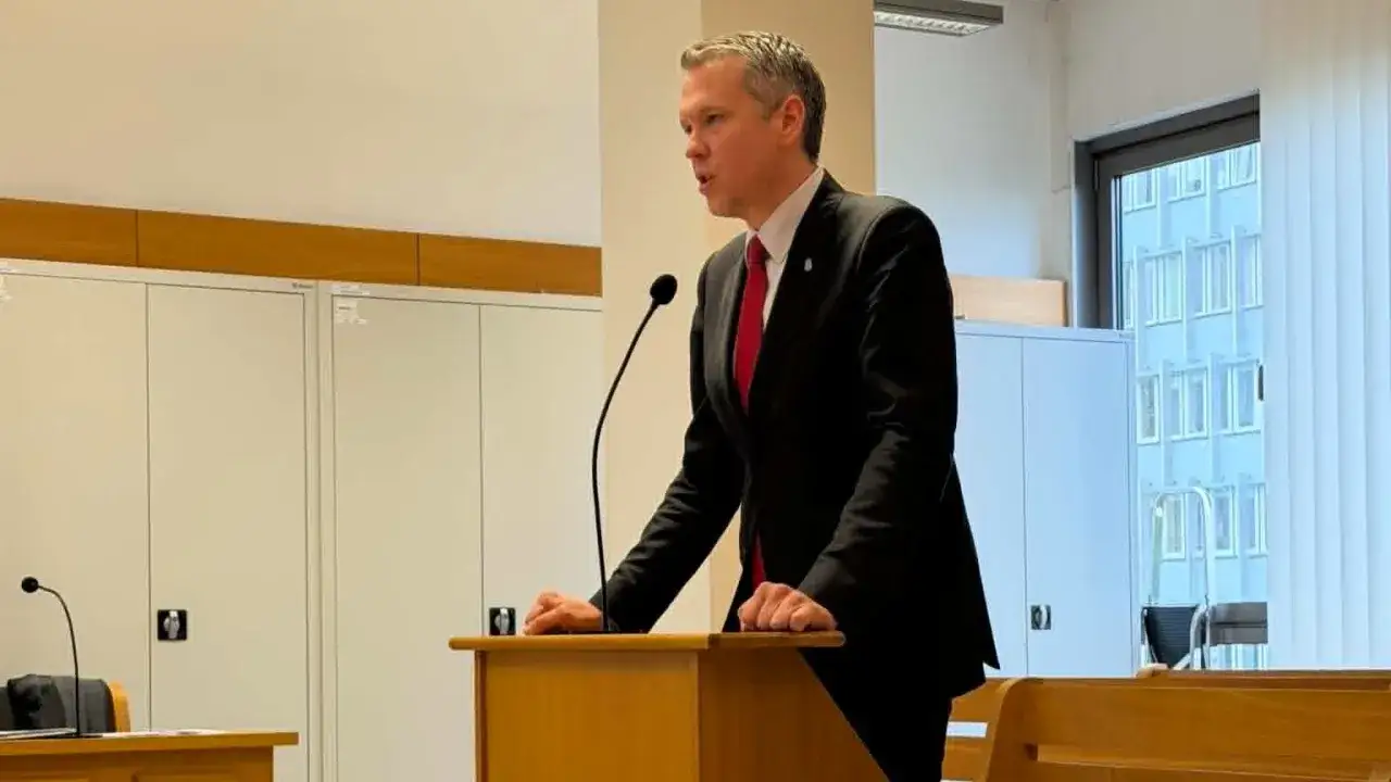 Mężczyzna w garniturze przemawia przy mównicy, przygotowując pozew w trybie wyborczym.