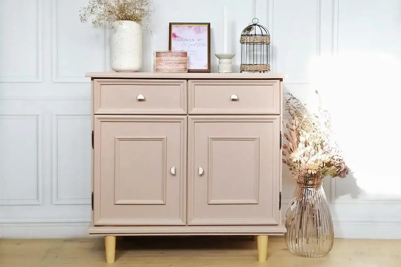 Meuble en bois peint, couleur rose poudr&eacute;, avec deux tiroirs et deux portes. D&eacute;cor&eacute; de fleurs s&eacute;ch&eacute;es et d'une cage &agrave; oiseaux.