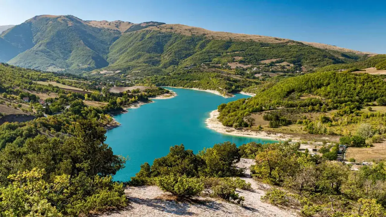 Il **lago di Fiastra** brilla di un azzurro intenso tra colline verdi e montagne maestose, un vero gioiello naturale.