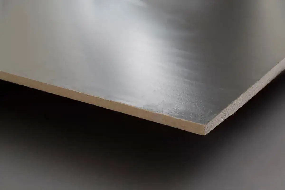 Superficie liscia e riflettente, simile a un **cappotto interno** metallico, su un pannello di legno grezzo.