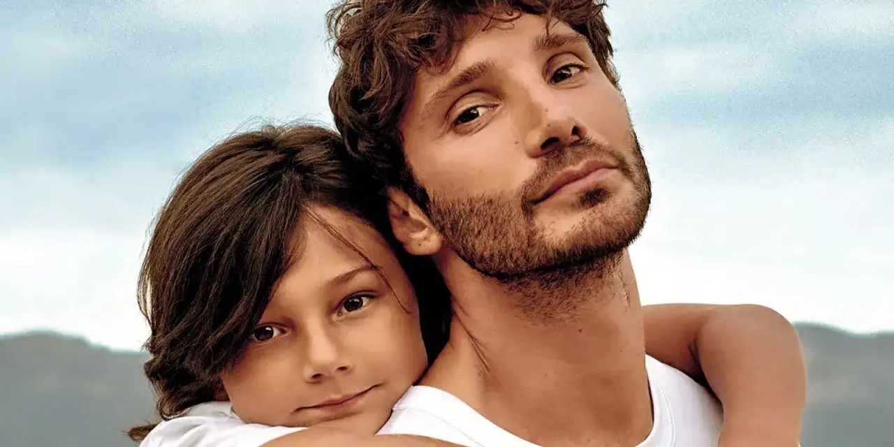Un bambino si appoggia a un uomo con la barba, un momento di tenerezza che ricorda Santiago de Martino.