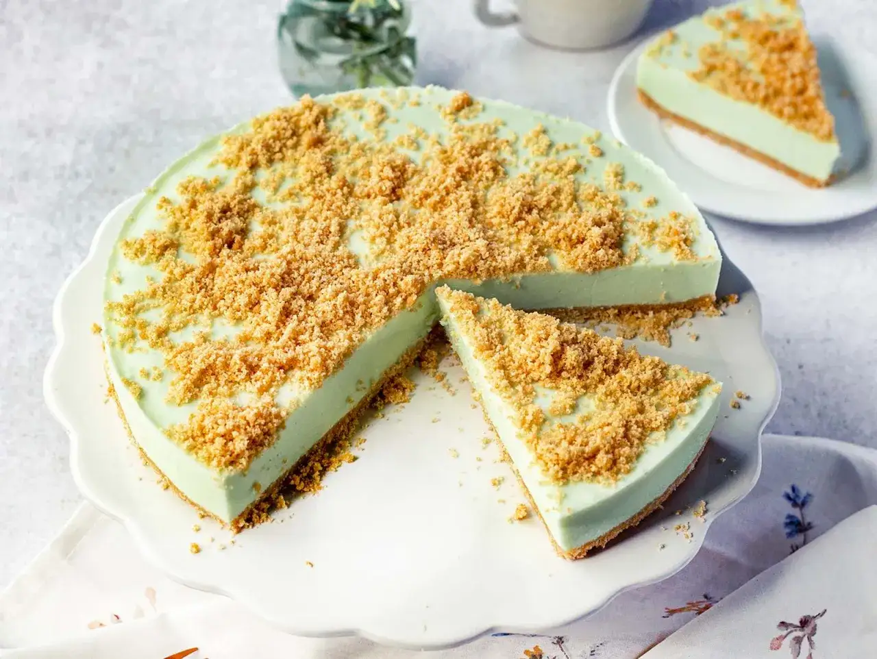 Eine cremige Philadelphia Torte Waldmeister mit knusprigem Keksboden und Streuseln. Ein Stück ist bereits angeschnitten.