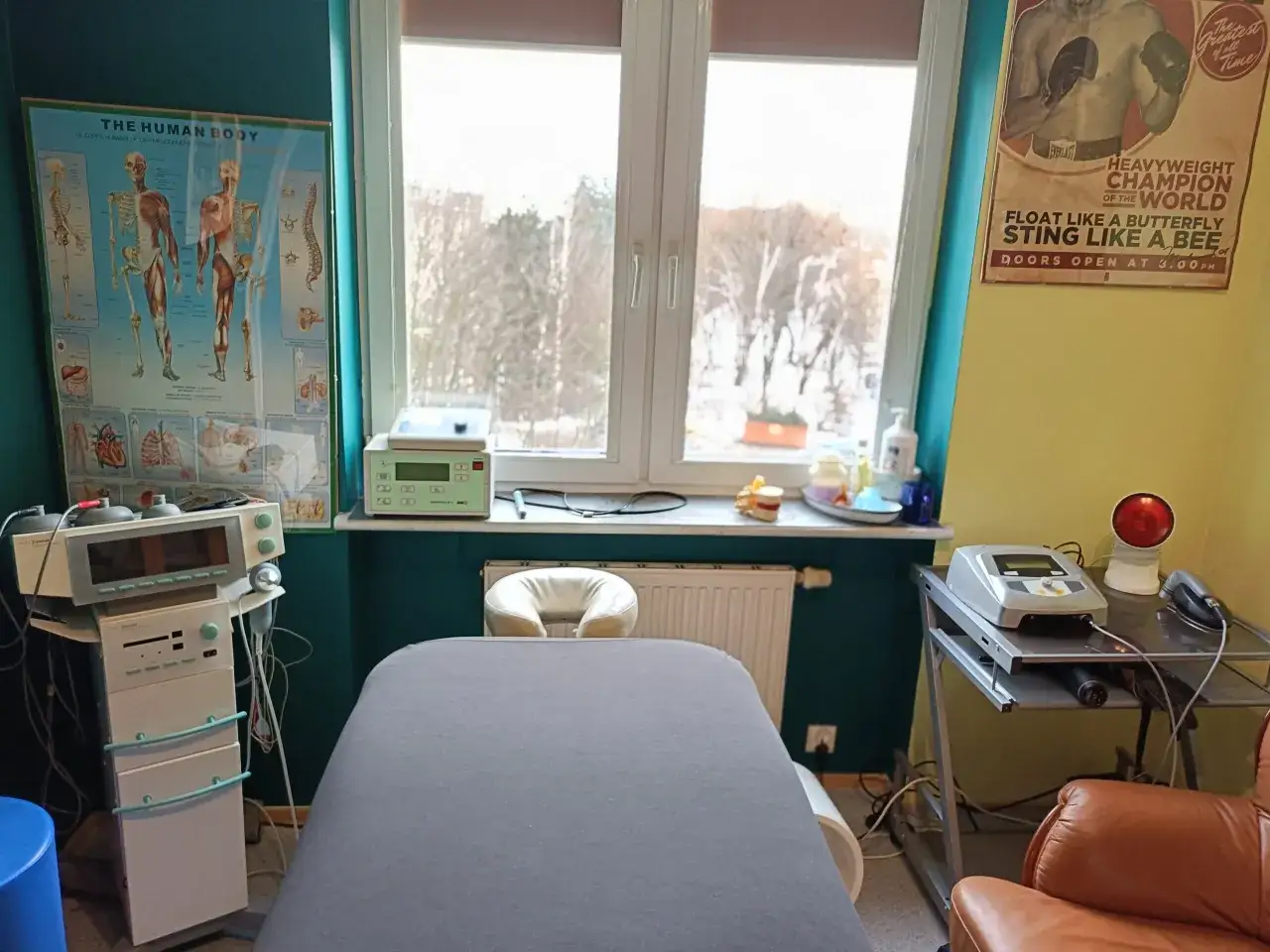 Gabinet fizjoterapii: łóżko, aparatura do elektroterapii, plakat anatomii człowieka. Fizykoterapia co to? To leczenie ruchem i zabiegami.