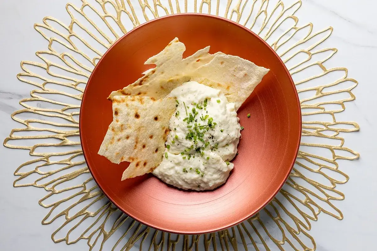 Deliziosa brandade di baccalà cremosa, guarnita con erba cipollina e servita con croccanti sfoglie di pane su un piatto ramato.