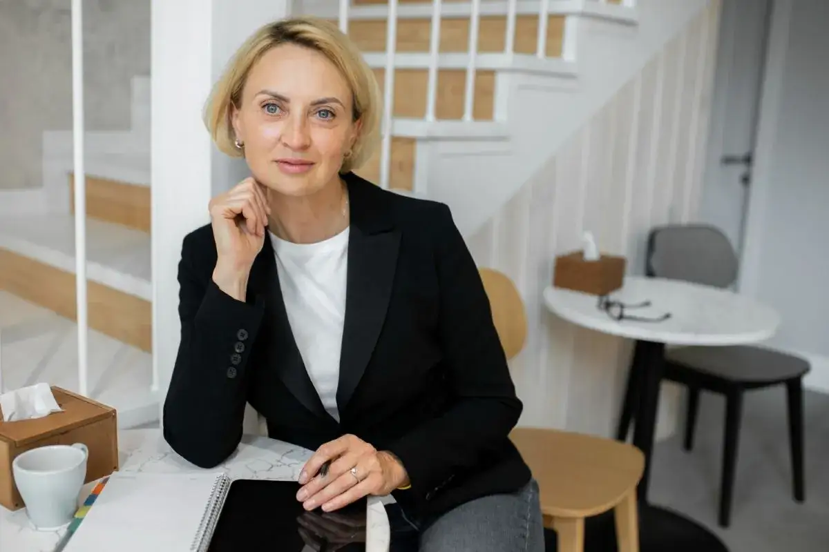 Donna bionda con giacca nera, pronta a cambiare lavoro a 50 anni, con tablet e taccuino.