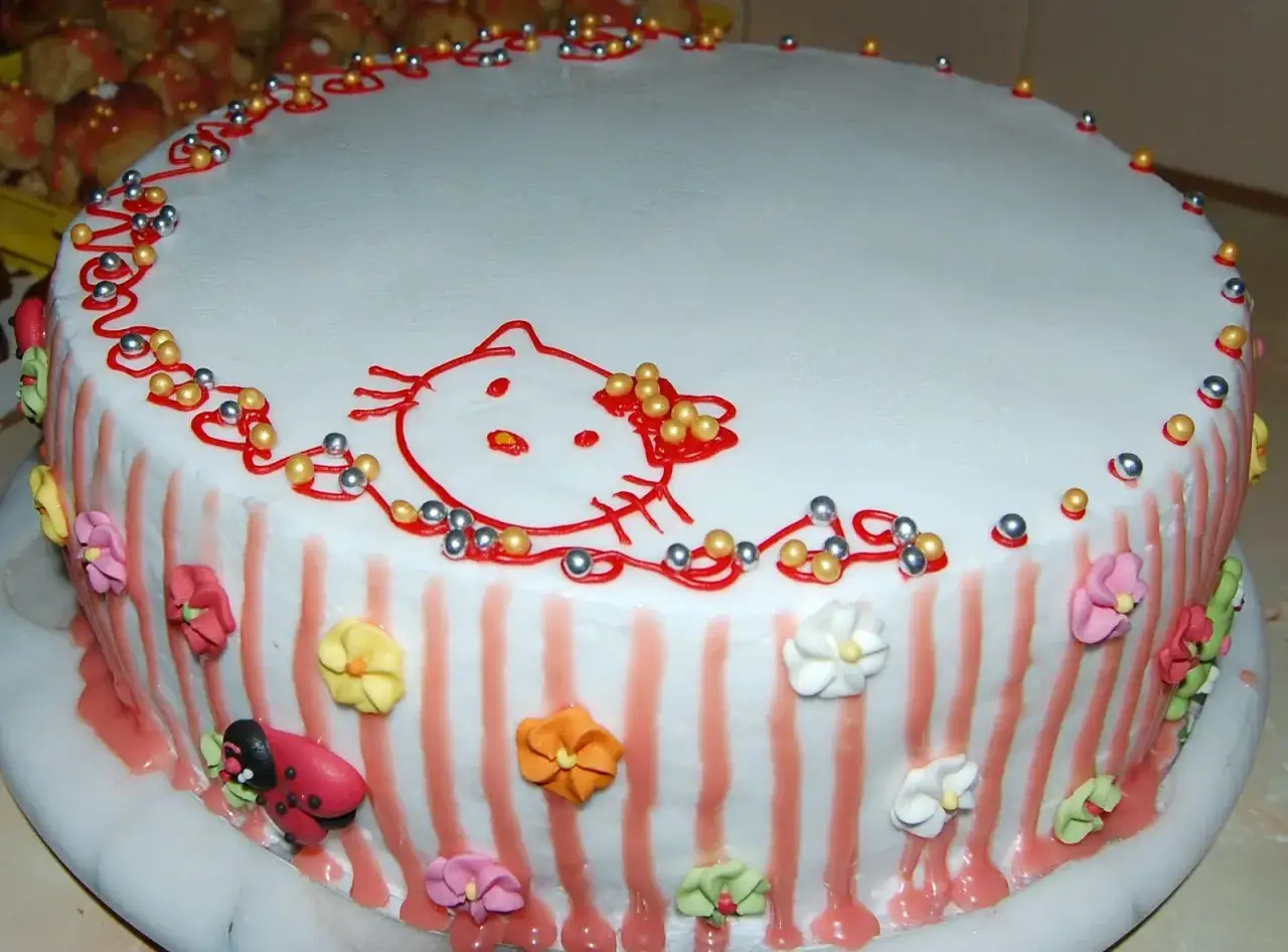 Tort ozdobiony Hello Kitty i kwiatkami z masy cukrowej. Dowiedz się, **fondant co to** jest i jak pięknie zdobi torty.