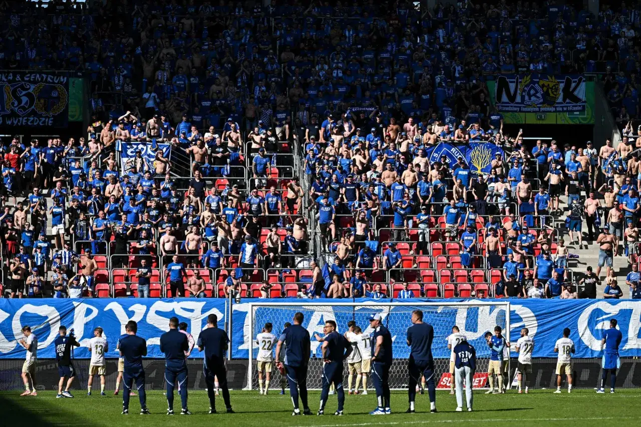 Piłkarze świętują awans do ekstraklasy na tle trybun pełnych kibiców w niebieskich barwach.
