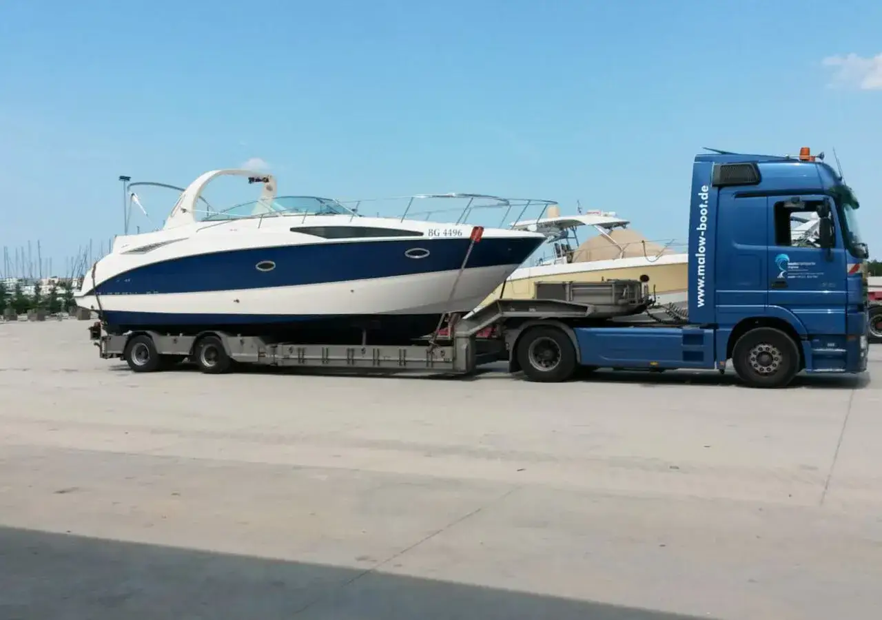 Blauer LKW transportiert ein weiß-blaues Boot auf einem Anhänger. Informieren Sie sich über bootstransport kosten.