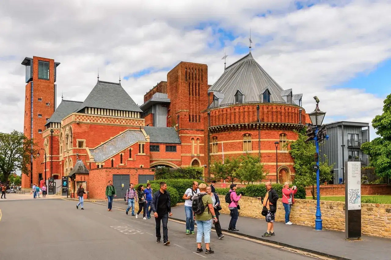 Ludzie spacerują ulicą w Stratford-upon-Avon obok ceglanych budynków Royal Shakespeare Company.