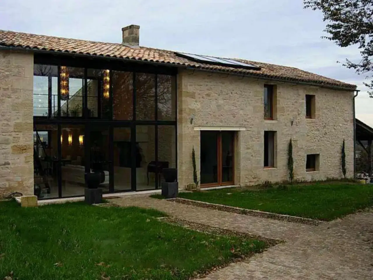 Maison en pierre avec grande façade vitrée, œuvre d'un architecte dplg. Panneaux solaires sur le toit.
