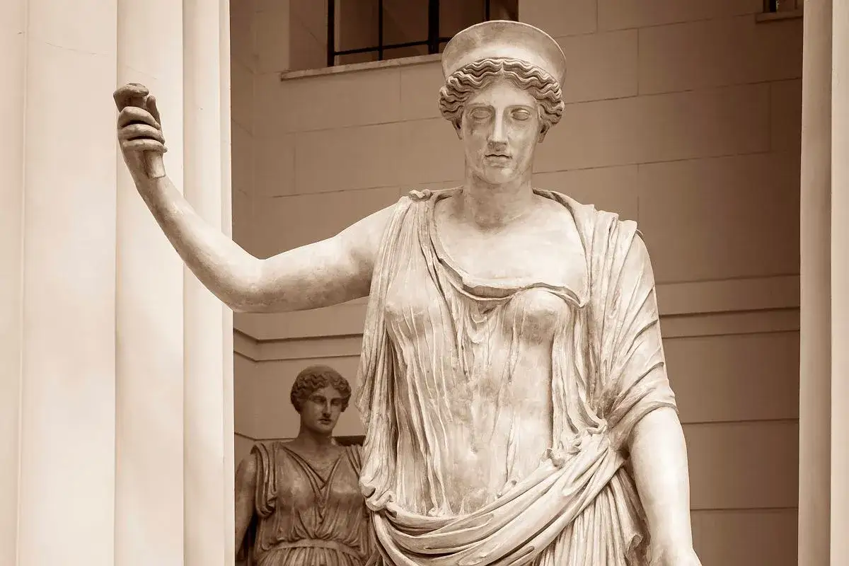 Posąg bogini z mitologii rzymskiej, z podniesioną ręką, w tle inna postać.