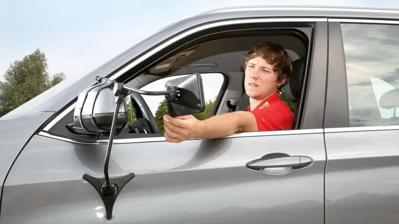 Mann justiert einen zus&auml;tzlichen Spiegel am Auto, der f&uuml;r Wohnwagen oft als wohnwagenspiegel pflicht gilt.
