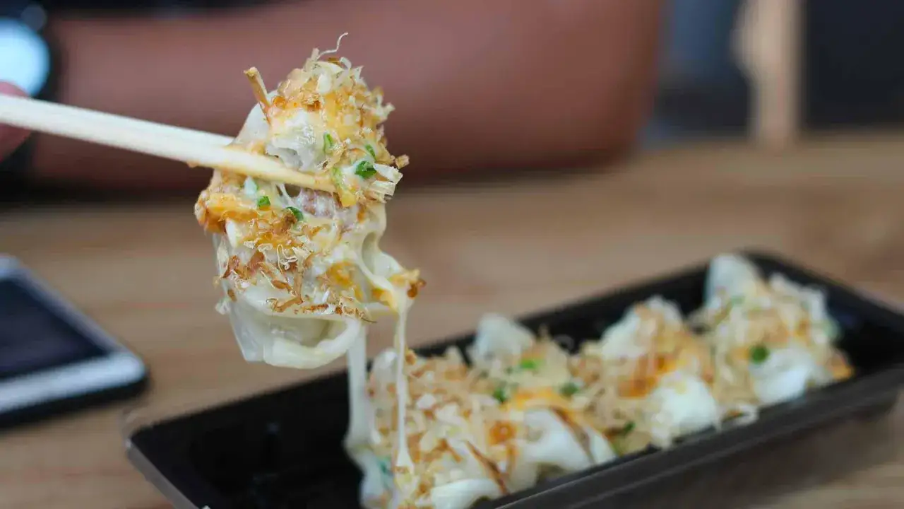 A chopstick lifts a cheesy, savory Japanese dish topped with bonito flakes.