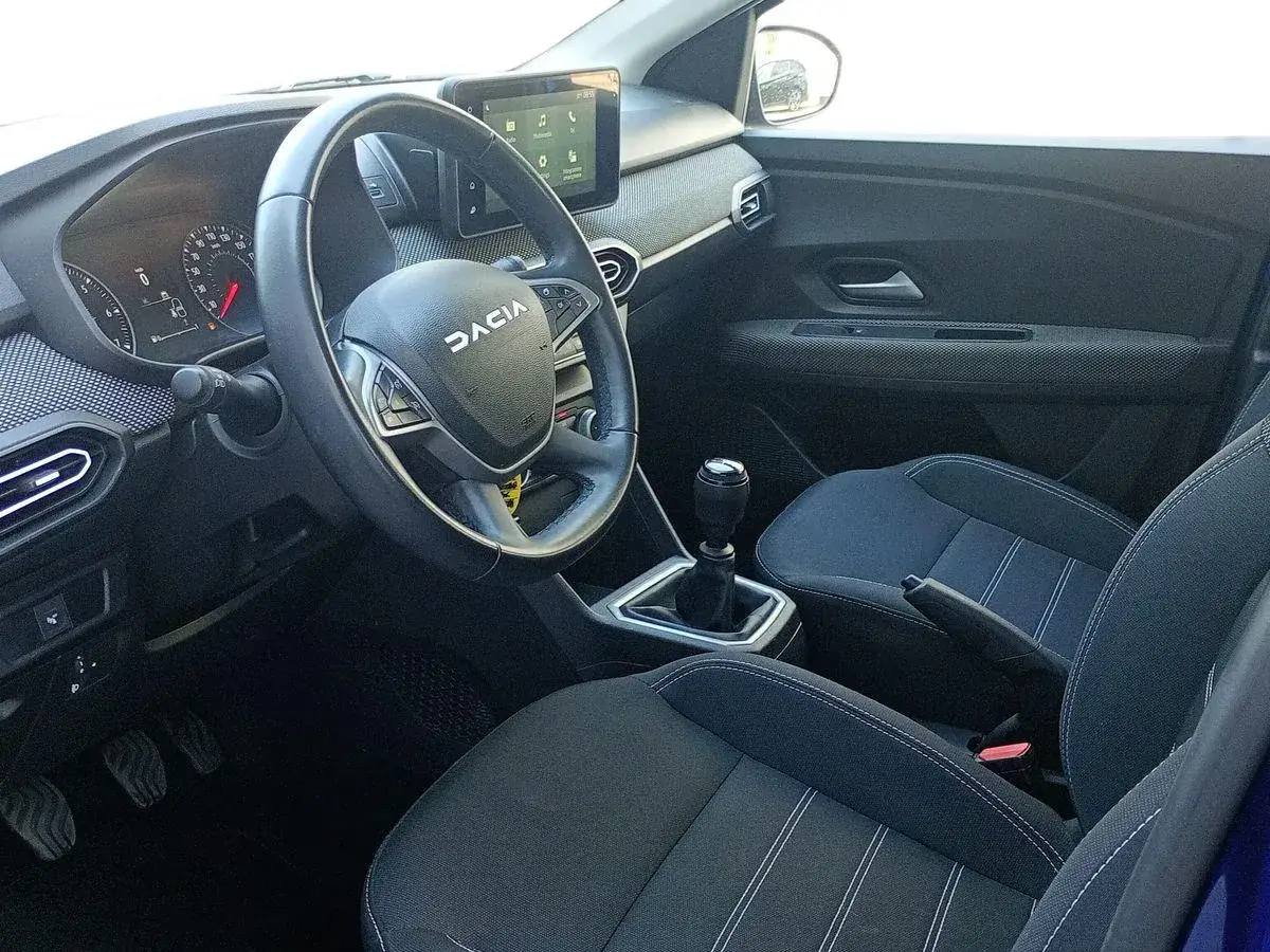 Interno di una Dacia Sandero 1500 diesel: volante, cruscotto digitale, cambio manuale e sedili con cuciture a contrasto.