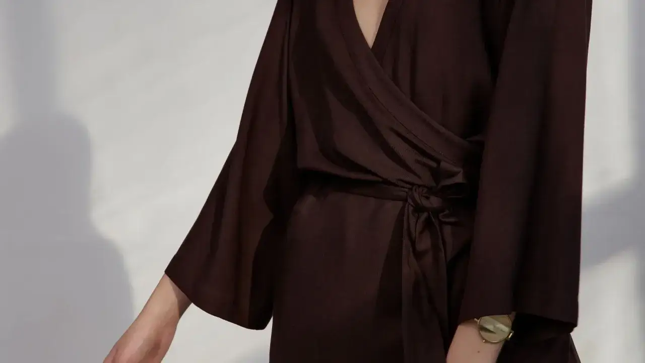 Elegancka sukienka kopertowa z wiskozy bawełnianej w odcieniu gorzkiej czekolady. Luźne rękawy i wiązanie w talii podkreślają sylwetkę.