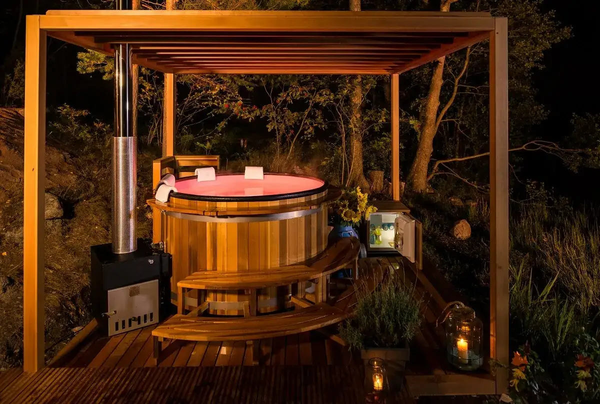 Drewniane jacuzzi z podświetloną wodą, pod zadaszeniem, w otoczeniu natury. Idealne miejsce na relaks, zastanawiasz się, ile razy w tygodniu można korzystać z jacuzzi?