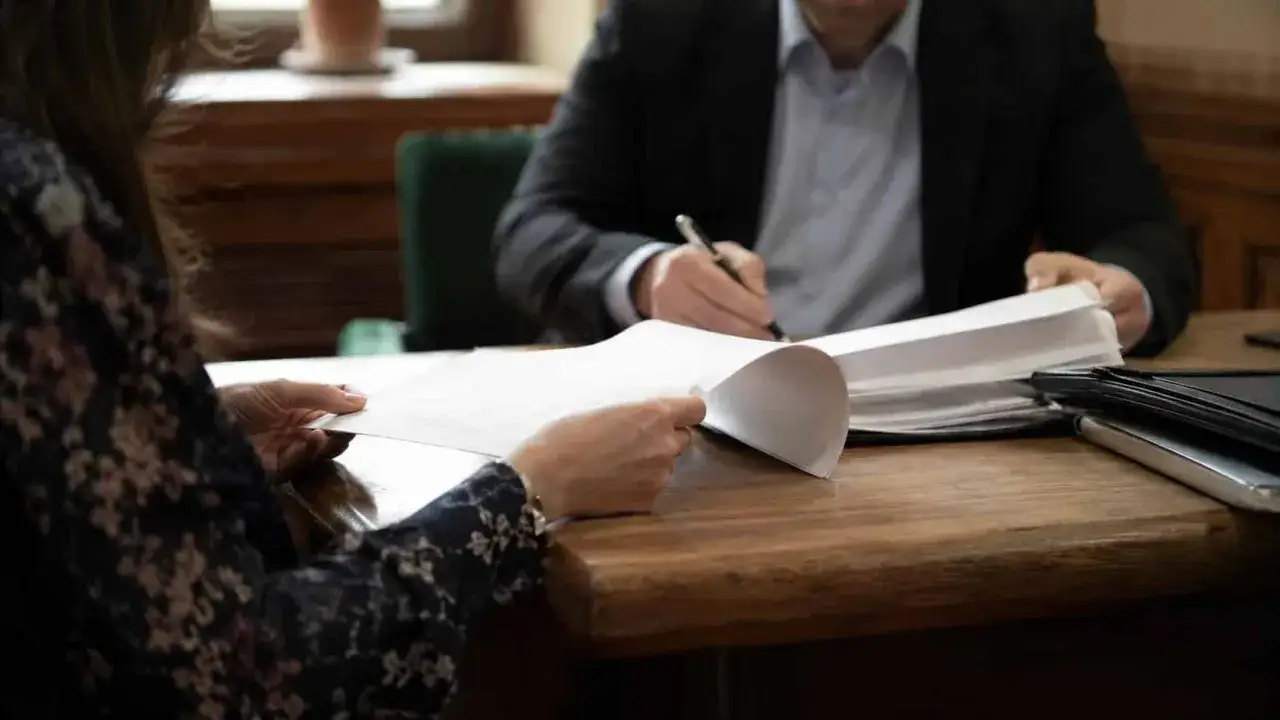 Rozmowa z prawnikiem o tym, jak odzyskać zaległe alimenty. Dwie osoby przeglądają dokumenty przy drewnianym stole.