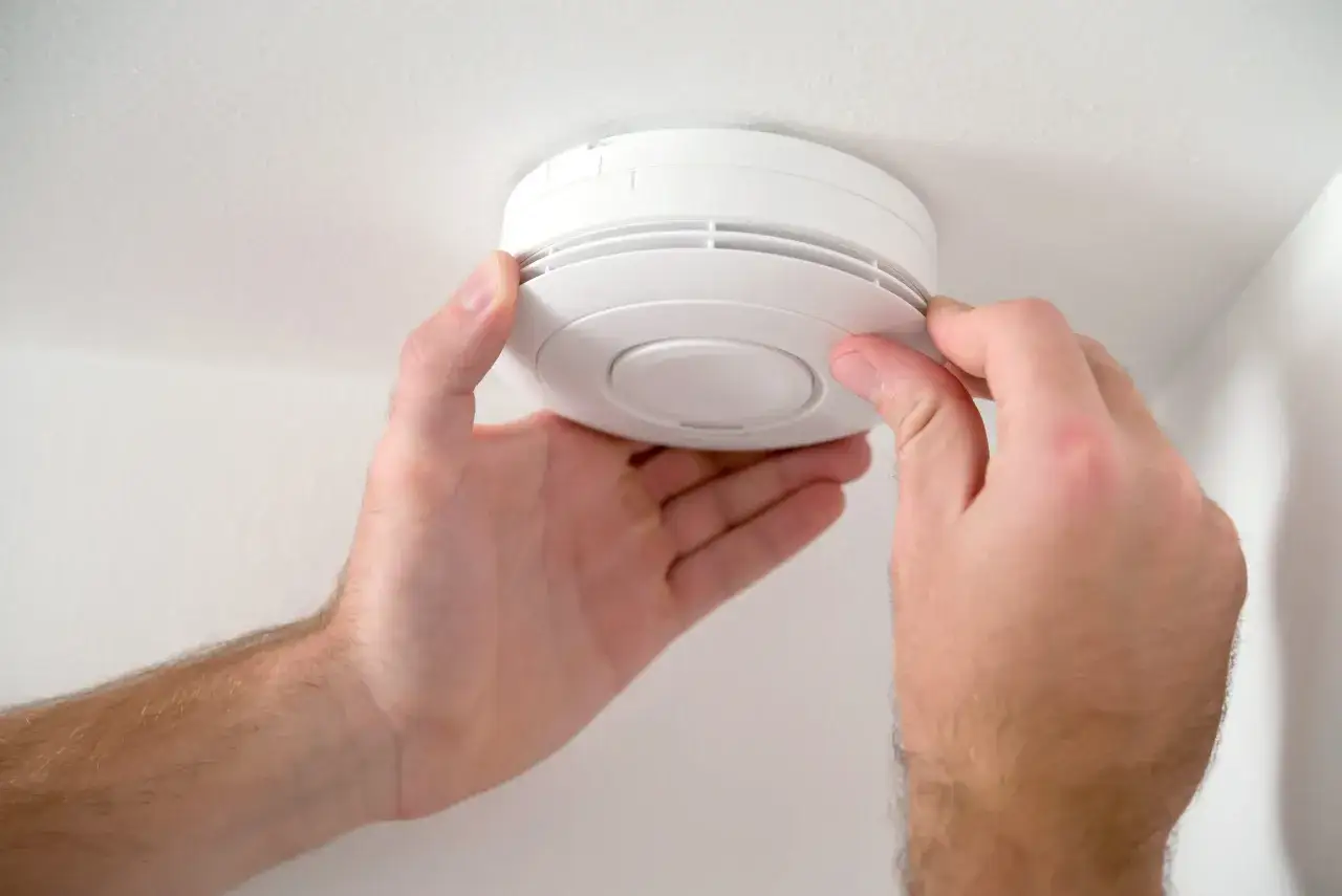 Mains installant un détecteur de fumée blanc au plafond. Pensez à vérifier la durée de vie détecteur de fumée pour votre sécurité.