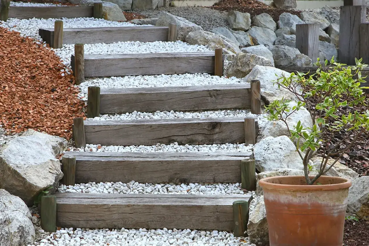 Eine einfache Gartentreppe selber bauen: Holzstufen mit Kies gef&uuml;llt, flankiert von Steinen und Rindenmulch.