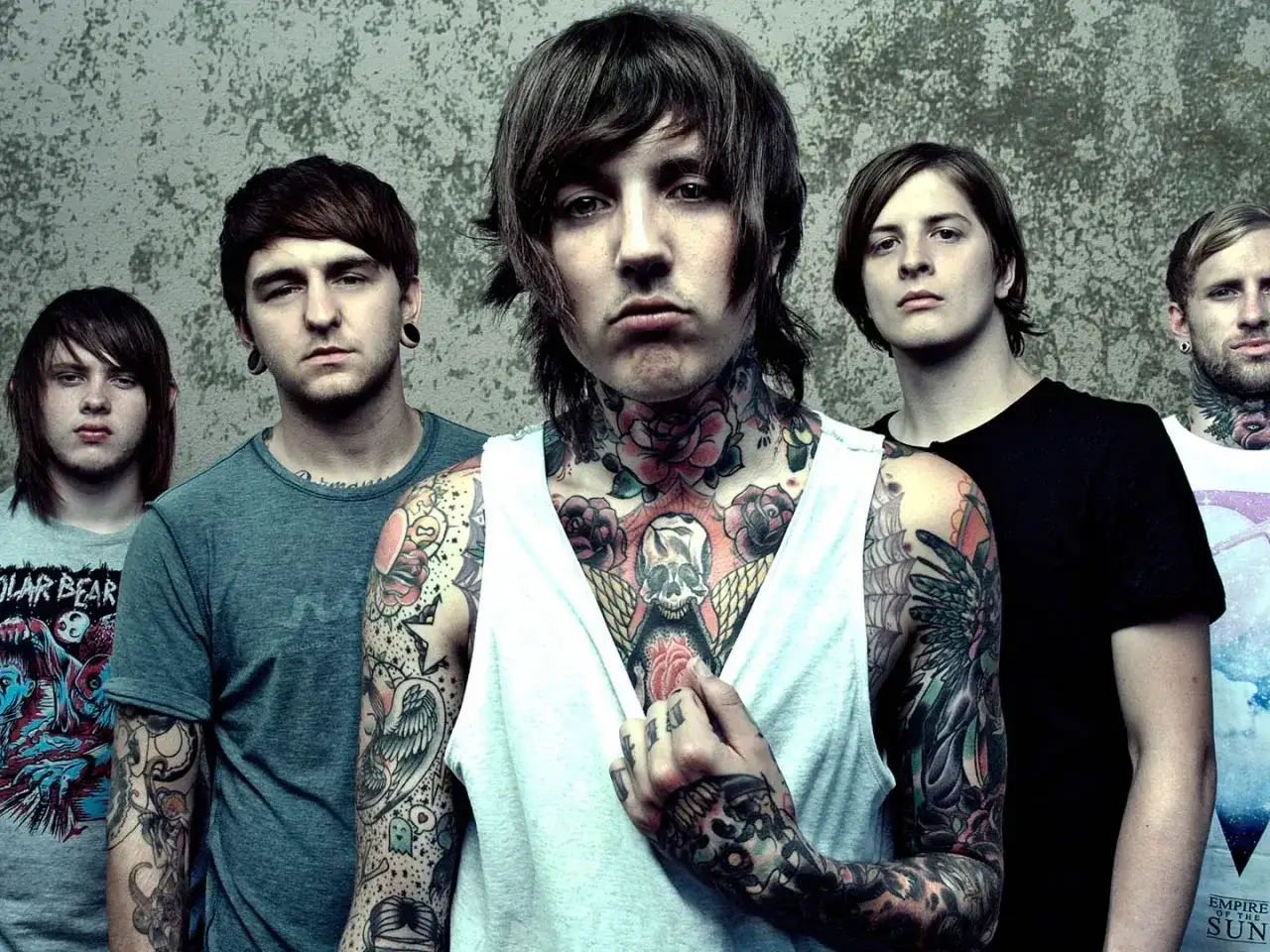 Bring Me The Horizon członkowie, z wokalistą w białej koszulce i licznymi tatuażami na szyi i rękach, pozują do zdjęcia.