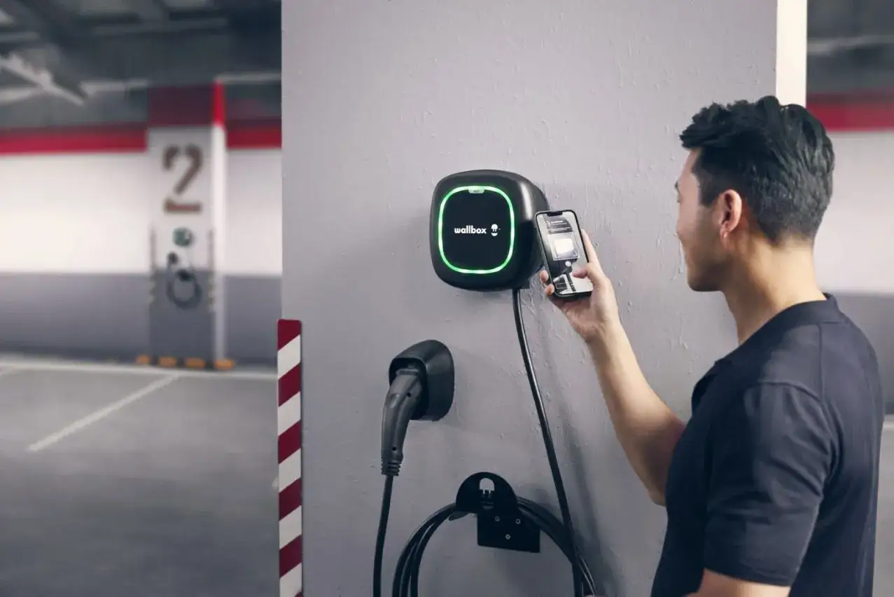 Hombre usa su móvil para activar el cargador de su primer vehículo eléctrico en un garaje.