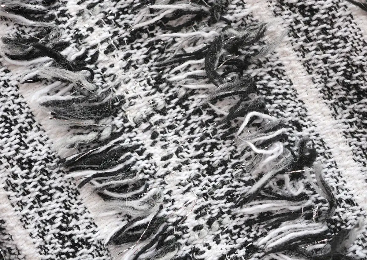 Texture d'un vêtement en matière élastique, tissage épais noir et blanc avec des fils argentés et des franges douces.