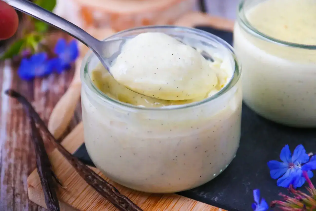 Délicieuse crème vanille recette, onctueuse et parsemée de grains de vanille, servie dans des pots en verre.