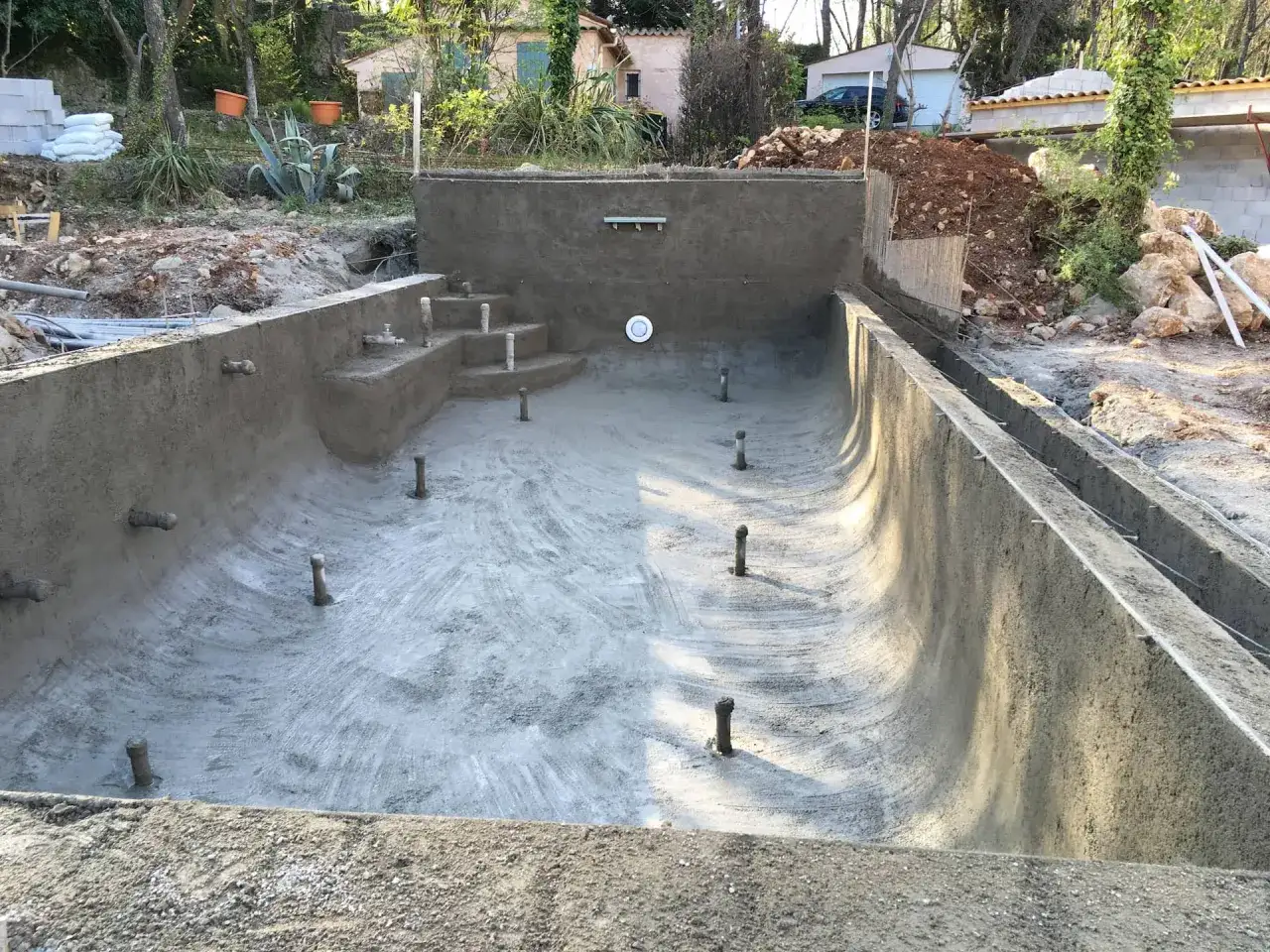 Piscine en béton en construction, prête pour l'étanchéité. Des escaliers et des buses sont visibles.