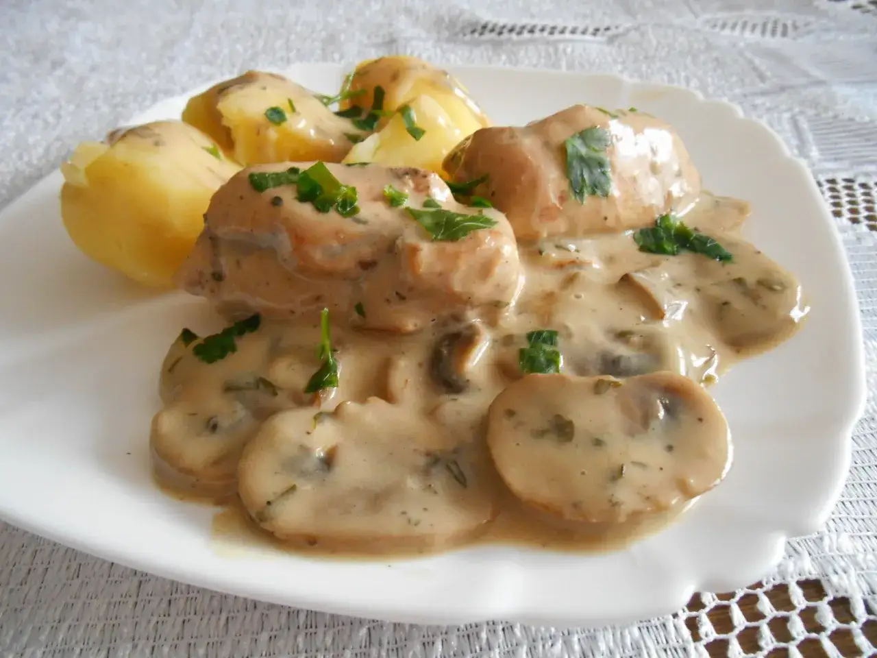 Pyszny kurczak w sosie pieczarkowym, podany z ziemniakami i posypany natką pietruszki.