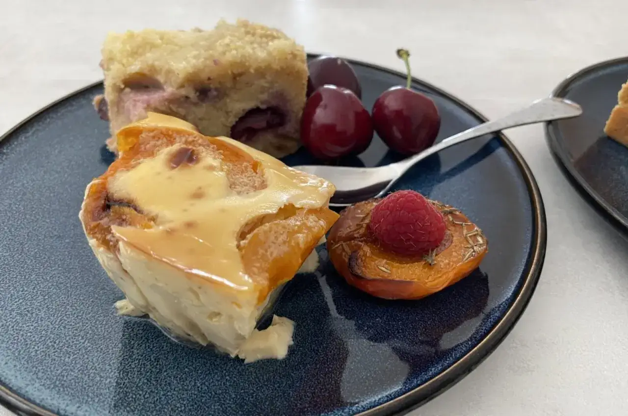 Un clafoutis moelleux aux abricots, servi avec des cerises et une pêche rôtie garnie d'une framboise.