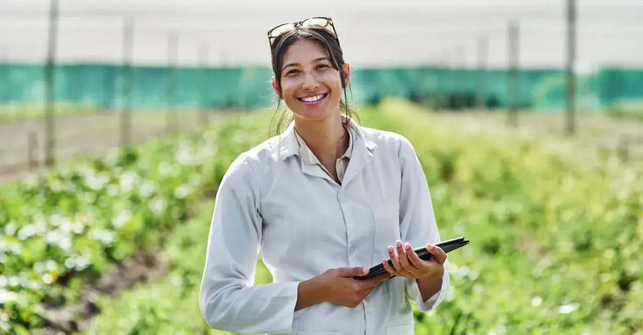 Un perito agrario sorride in un campo, tenendo un tablet.