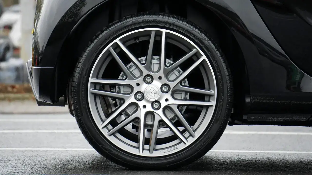 Błyszczące, czarne nadkole samochodu z felgą Brabus i oponą na mokrej nawierzchni.