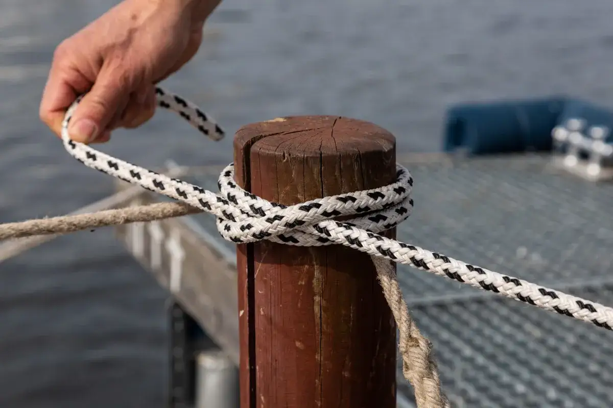 Hand knotet ein Seil um einen Holzpfahl, um ein Boot festzumachen.