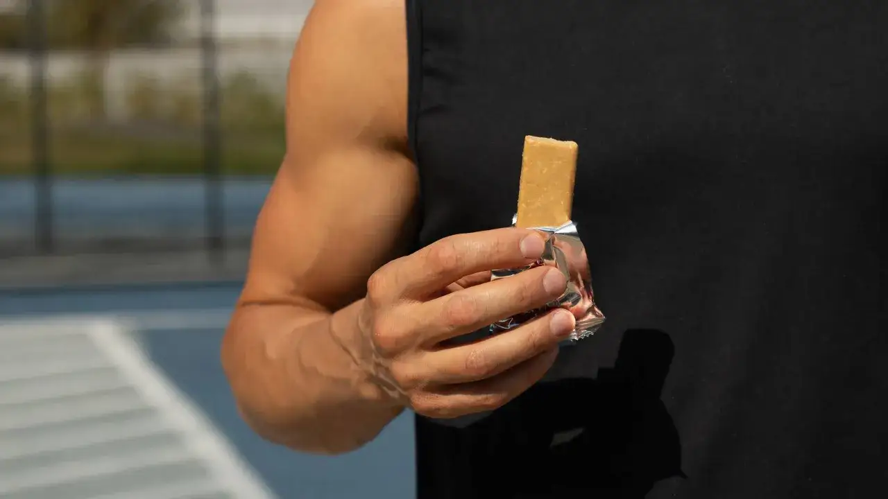 Muskul&ouml;ser Mann h&auml;lt einen Proteinriegel. Perfekt, wann proteinriegel essen nach dem Training.
