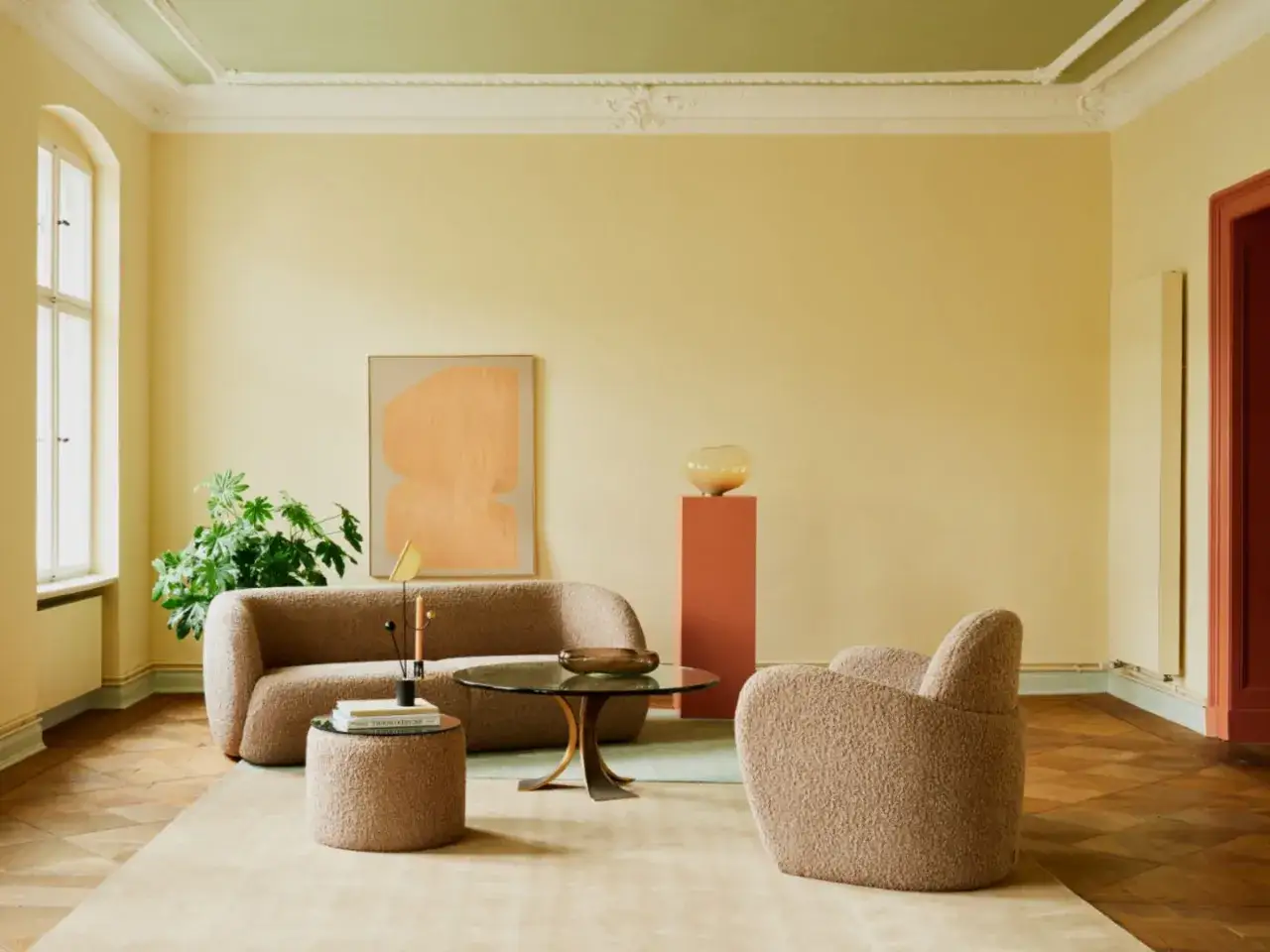 Ein Wohnzimmer mit gelben Wänden und einer grünen Decke, die frisch gestrichen wurde. Ein beiger Teppich liegt auf dem Parkettboden.