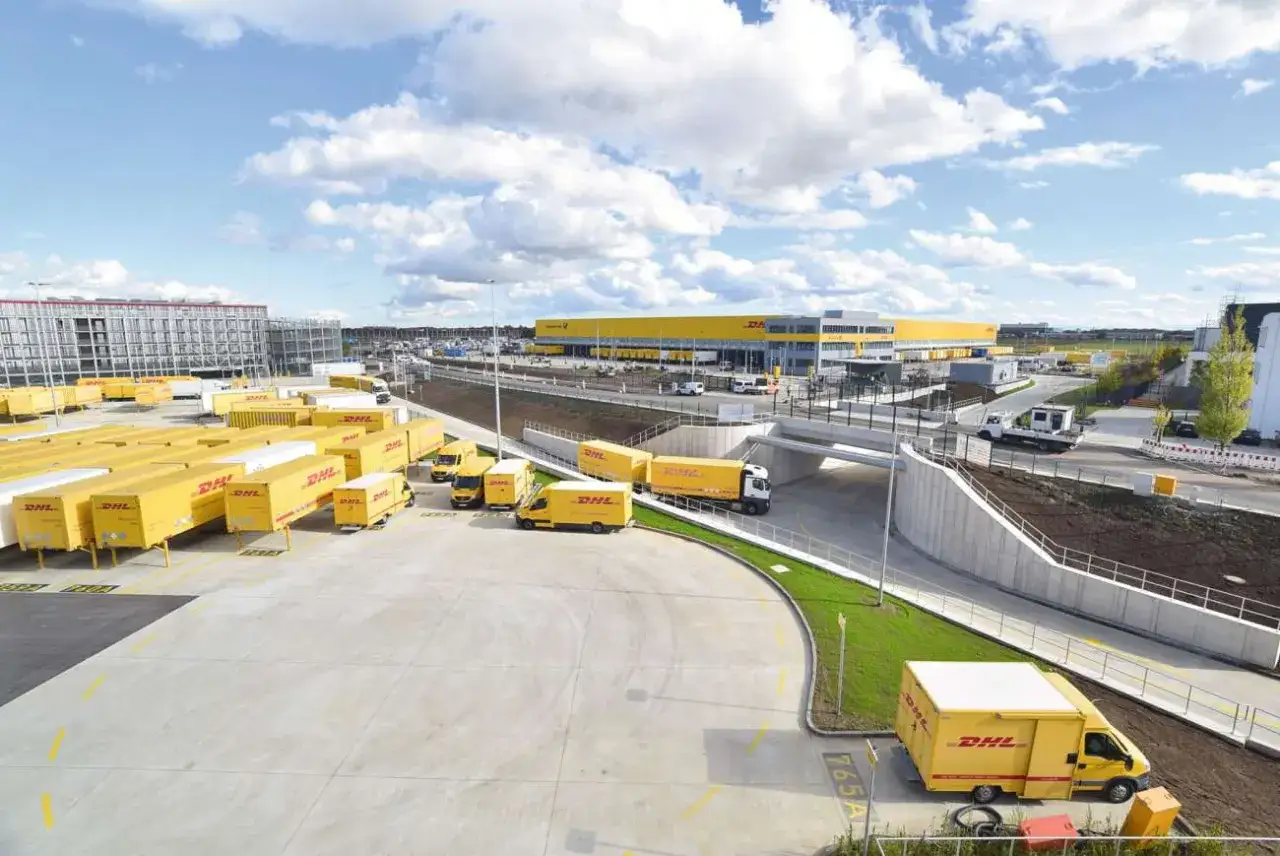 Gro&szlig;er DHL-Komplex mit vielen gelben Lieferwagen und Anh&auml;ngern. Ein moderner **destination hub deutsch** f&uuml;r Pakete.