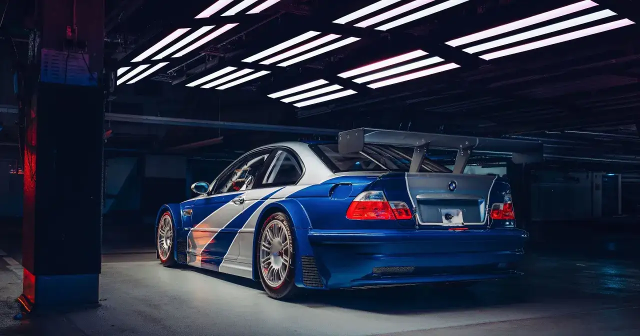 Niebiesko-białe BMW M3 GTR z wielkim spojlerem, gotowe do wyścigu w mrocznym garażu.